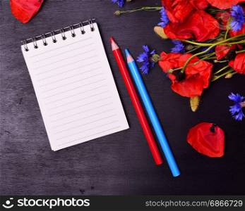 blank open notebook in a line on a black wooden background, near a bouquet of a field flower and two pencils