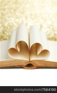 Blank pages of open book rolled in heart shape on glitter background. Book pages in heart shape