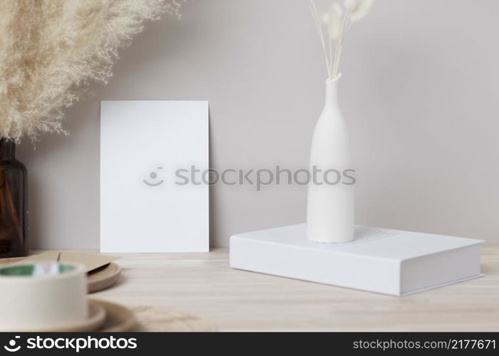 Blank paper card, greeting card mock up. decoration with dried Bunny Tail and pampas grass, Front view, Beautiful Bunny Tail grass in vase and white book on wood table and beige cement wall background