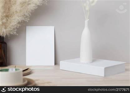 Blank paper card, greeting card mock up. decoration with dried Bunny Tail and pampas grass, Front view, Beautiful Bunny Tail grass in vase and white book on wood table and beige cement wall background