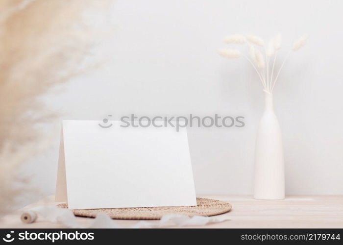 Blank paper card, greeting card mock up. decoration with dried Bunny Tail and p&as grass, Front view, Beautiful Bunny Tail grass in vase on wood table and beige cement wall background 