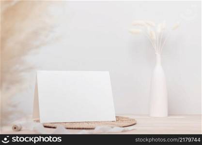 Blank paper card, greeting card mock up. decoration with dried Bunny Tail and p&as grass, Front view, Beautiful Bunny Tail grass in vase on wood table and beige cement wall background 