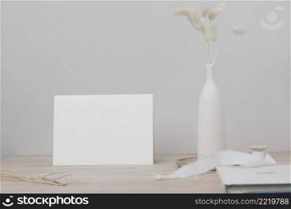 Blank paper card, greeting card mock up. decoration with dried Bunny Tail, Front view, Beautiful Bunny Tail grass in vase on wood table and beige cement wall background