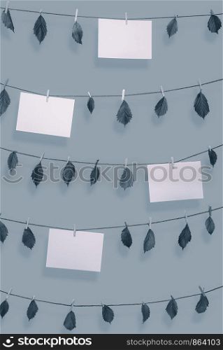 Blank paper notes and dried leaves hanging on clotheslines with wooden clips. Paper sheet frames in blue monochrome color. Environment concept. Nature