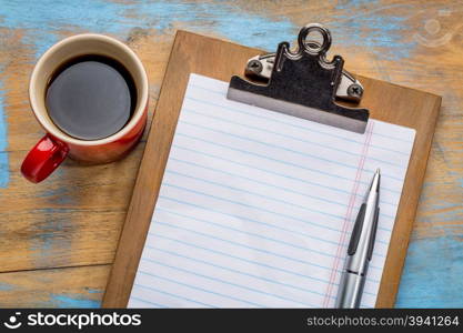 blank paper on clipboard with a pen and coffee against grunge wood desk - office concept