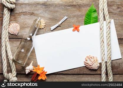 Blank paper sheet on weathered wood background with rope, shells, leaf and flowers