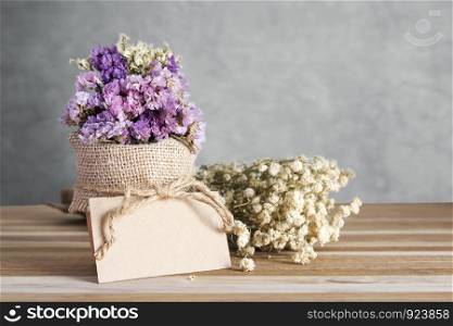 Blank paper tag and dry flowers on wooden table