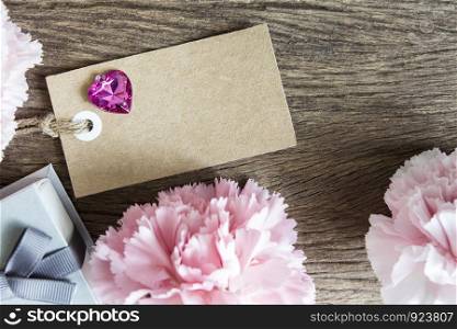 Blank paper tag with carnation flowers on wooden background