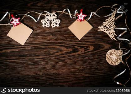 Blank, photo, instant, small paper hanging. Christmas tree ornaments with ribbons, snowflakes, bells on brown, structural wood background. flat lay. top view, frame with space for text. happy holidays