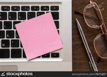Blank pink notepad putting on laptop. pen and eye glasses on wood table