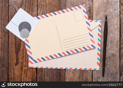 Blank post card with envelope, stamps and coins on wooden table