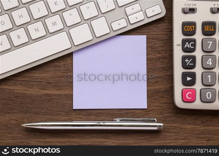 Blank purple notepad putting under keyboard. Pen and calculator on wood table