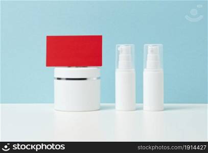 blank red paper business card and a set of plastic white containers for cosmetics on a blue background. Brand concept, promotion and product demonstration
