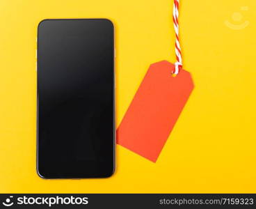 Blank red tag label shopping concept and smart phone blank screen, with copy space on yellow background