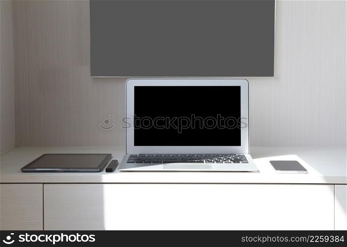 blank screen laptop computer and smart phone and digital tablet and stylus pen and poster is on wooden desk as workplace concept
