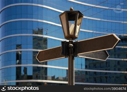 Blank signpost with ancient lamp against business building