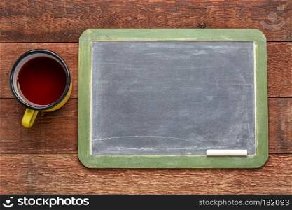 blank slate blackboard with a chalk against rustic barn wood table with metal cup of tea