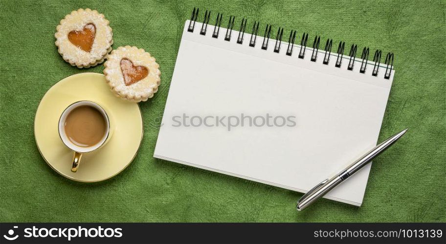 blank spiral art sketchbook against textured green bark paper, flat lay with coffee and heart cookies, love or romance greeting card concept