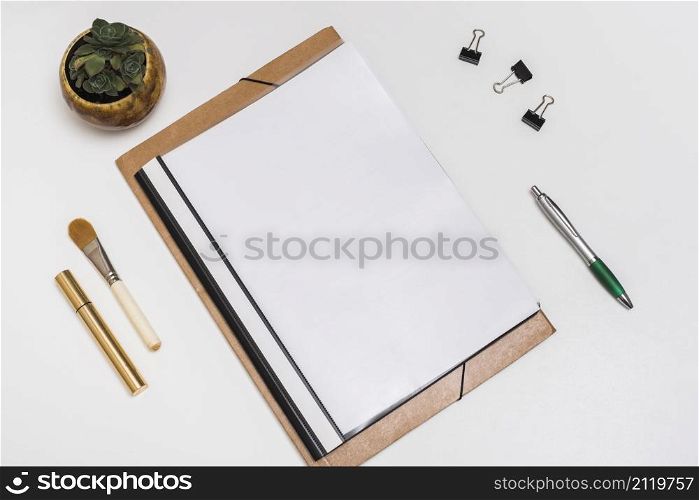 blank spiral notebook with make up brush mascara paper clips pen with potted plant white desk