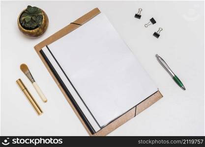 blank spiral notebook with make up brush mascara paper clips pen with potted plant white desk