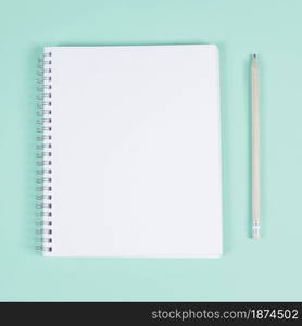 blank spiral notebook with pencil turquoise background
