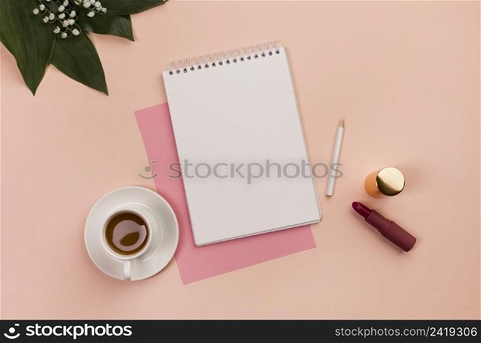 blank spiral notepad pencil lipstick coffee cup leaves peach background