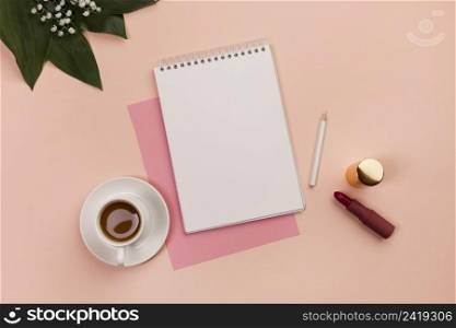 blank spiral notepad pencil lipstick coffee cup leaves peach background
