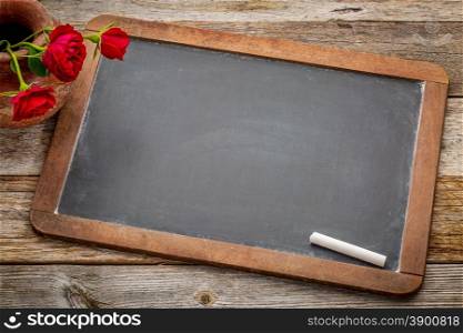 blank vintage slate blackboard with white chalk and red roses against rustic wood