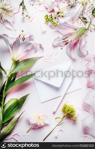 Blank white envelop with pencil and various decoration equipment and flowers on pink pale table background, top view. Festive Invitation , Creative greeting and holiday, concept