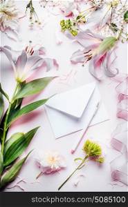 Blank white envelop with pencil and various decoration equipment and flowers on pink pale table background, top view. Festive Invitation , Creative greeting and holiday, concept