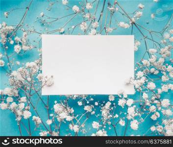 Blank white greeting card on little white flowers at turquoise blue background, top view, mock up