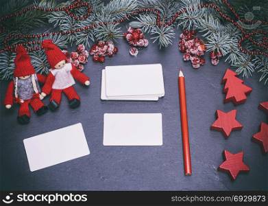 blank white paper business cards on a black background and a red pencil among the Christmas decor