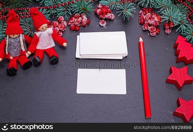 blank white paper business cards on a black background and a red pencil among the Christmas decor, top view