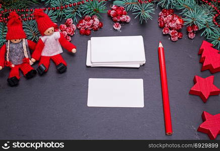 blank white paper business cards on a black background and a red pencil among the Christmas decor, top view