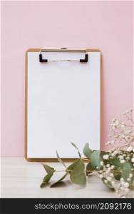 blank white paper clipboard with leaves baby s breath flowers wooden desk against pink background
