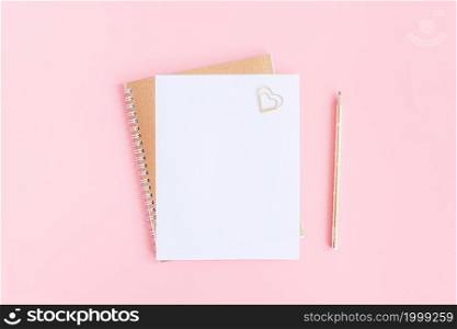 Blank white sheet on spiral golden notepad with paper clip heart and pencil on pink pastel background. Mock up for your text and design. Top view Flat lay Minimal style.. Blank white sheet on spiral golden notepad with paper clip heart and pencil on pink pastel background. Mock up for your text and design. Top view Flat lay Minimal style