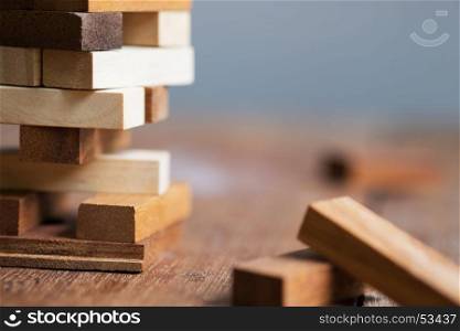 Blank wooden block leaning on a structure made of many other blocks with several of them still lying scattered on a textured rustic wooden desk. Conceptual of leisure game or start up business