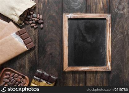 blank wooden slate with cocoa beans chocolate bars wooden table
