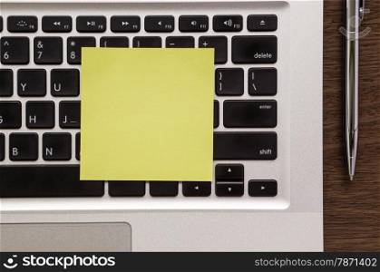 Blank yellow notepad putting on laptop keyboard with pen on wood table