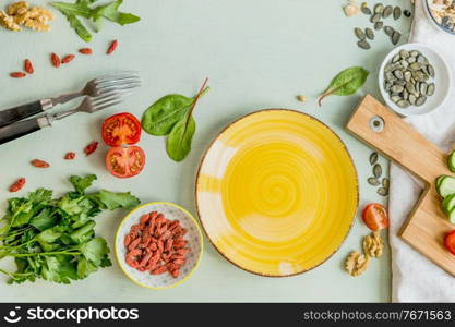 Blank yellow plate on green table with forks and healthy salad ingredients. Top view. Healthy lunch preparation