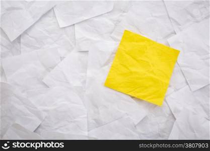blank yellow sticky note against background of white crumpled notes