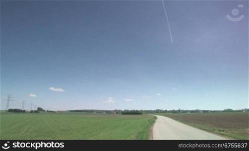 Blauer Himmel, Feldweg und AckerflSche, Schwenk nach links auf Hochspannungsleitung vor Dorf in lSndlicher Umgebung