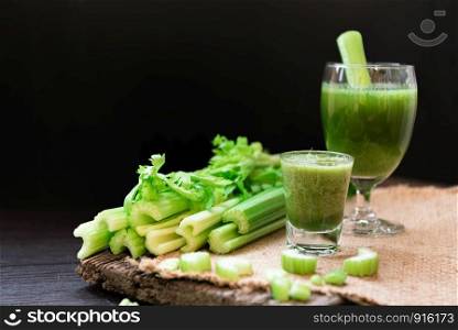 Blended Celery juice in welcome drink glass and bunch of fresh celery stalk on wooden table with leaves on black background. Food and ingredients of healthy vegetable. Freshness herbal for dieting
