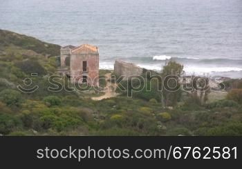 Blick auf ein altes Haus direkt am Ufer von einem Meer mit Wellen.