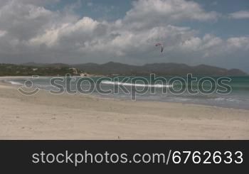 Blick auf einen Strand mit einem Kitesurfer im Hintergrund bei Sonne.