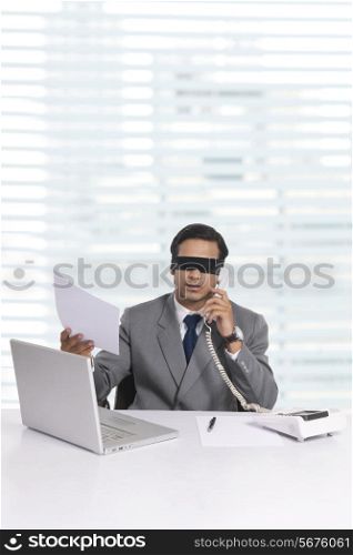 Blindfolded young businessman working at office desk