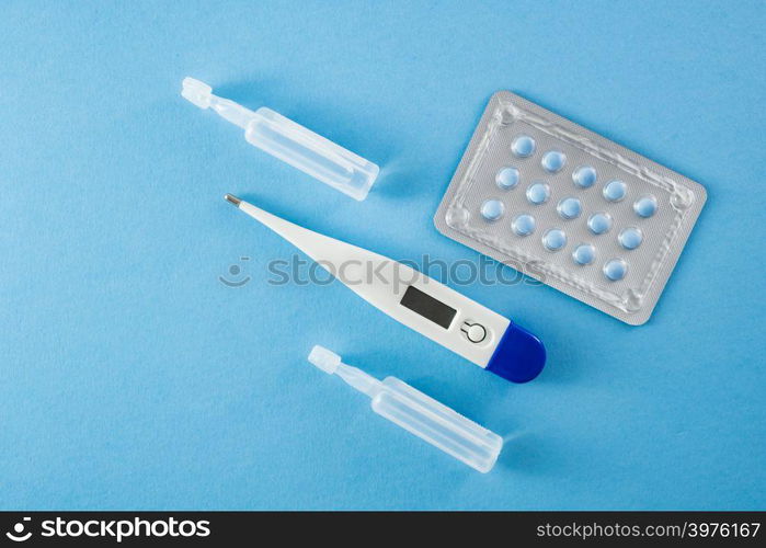 Blister pack of blue pills, ampoules and thermometer on blue background- healthcare and medical concept