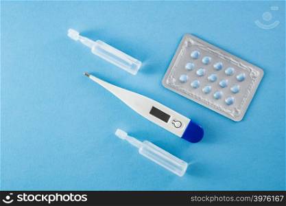 Blister pack of blue pills, ampoules and thermometer on blue background- healthcare and medical concept