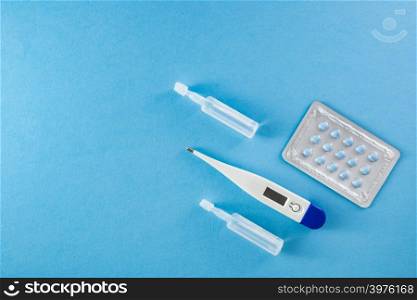 Blister pack of blue pills, ampoules and thermometer on blue background with copyspace- healthcare and medical concept