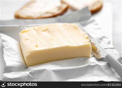 Block of butter with butter knife in a open pack.  Buttering bread